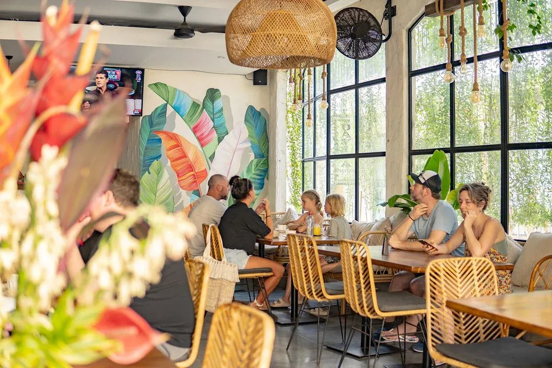 cafe dining room with mural, tables, woven chairs, and service activity